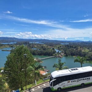 Modern Colsetrans A/C bus transporting travelers on the winding road overlooking the beautiful Guatape reservoir and mountains.