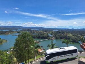Modern Colsetrans A/C bus transporting travelers on the winding road overlooking the beautiful Guatape reservoir and mountains.
