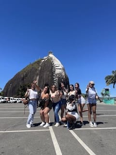 Diverse group of seven happy travelers posing in front of the magnificent Piedra del Peñol rock, Guatape.