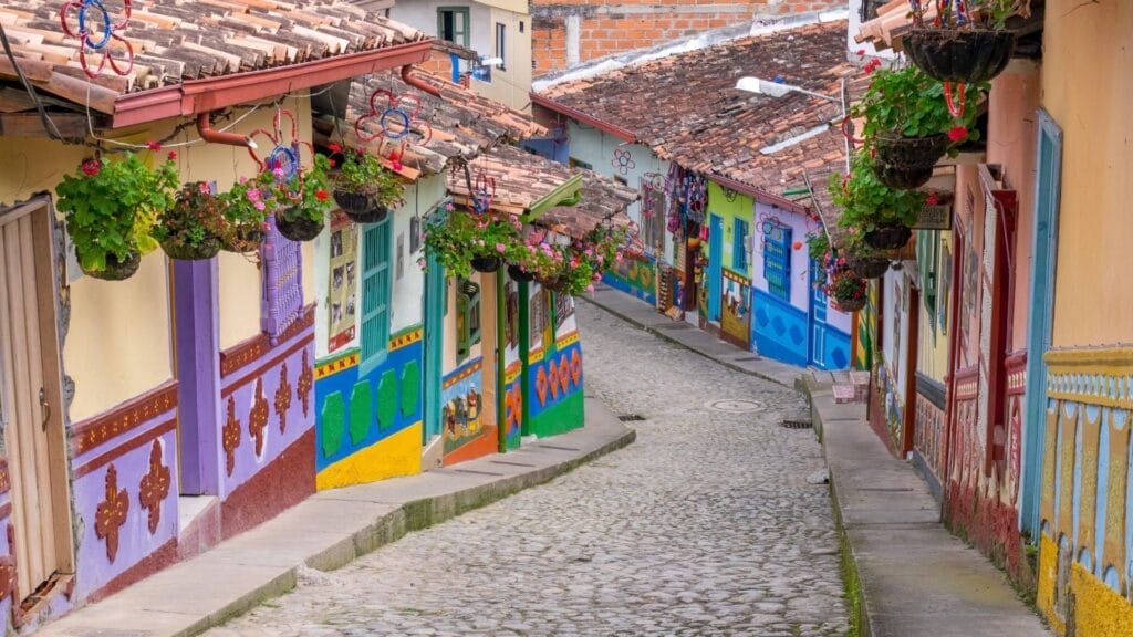 View down a narrow, curving cobblestone street in Guatapé, showcasing traditional colonial architecture, colorful Zócalos, and hanging flower baskets.