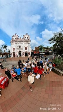 Large group of happy tourists taking a wide-angle selfie in the main square of Guatape, with the historic church (Parroquia) visible behind them.
