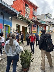 Group of tourists on a guided walking tour of Guatape town, standing on a cobblestone street near the famously colorful Zócalo-style buildings.