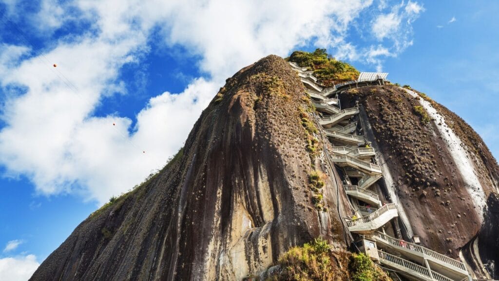 Extreme low-angle view of the massive Piedra del Peñol rock, emphasizing the scale and the winding 700-step staircase built into its face.