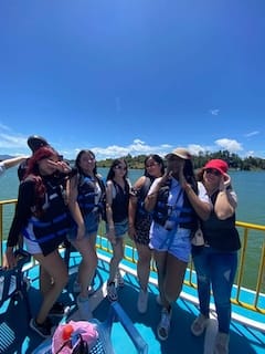 Group of female travelers wearing life vests and enjoying the scenic boat tour on the Guatape reservoir under a clear blue sky.